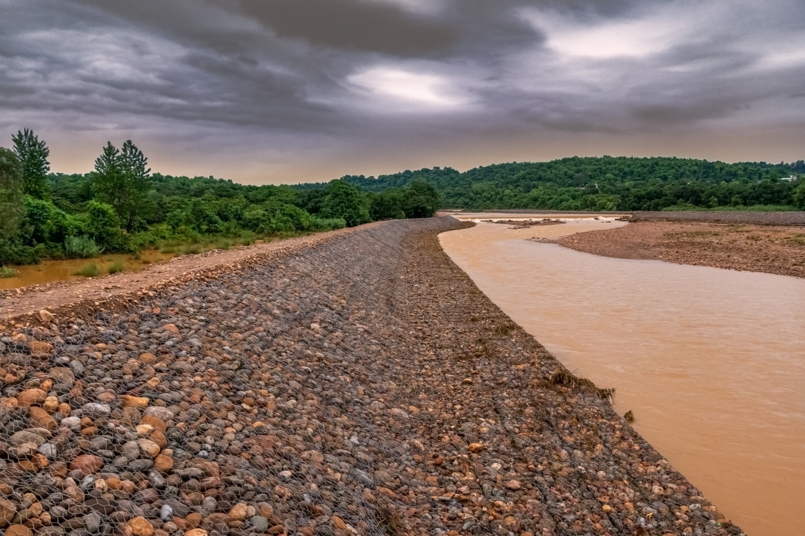 Gabion, Cages Filled with Rocks Placed at Riverbank to Control Erosion, Background of Dark Sky and River dirty water, after rain in rainy season landscape. Gabion, Cages Filled with Rocks Placed at Riverbank to Control Erosion, Background of Dark Sky and River dirty water, after rain in rainy season landscape.